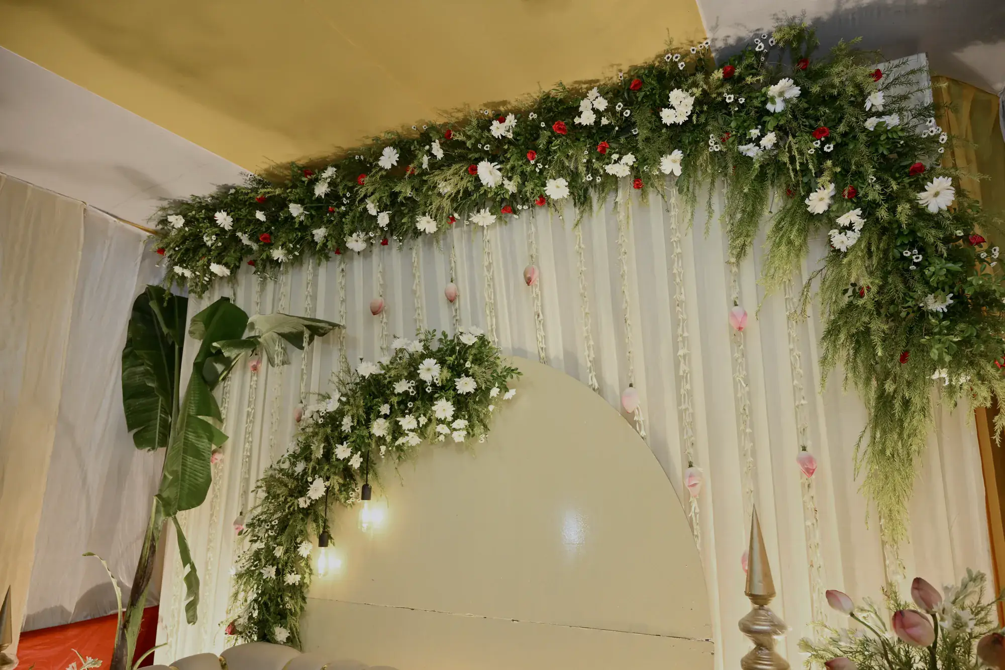A stage canopy of white florals and greenery, lit warm for the guests' arrival