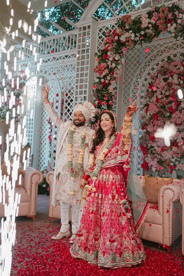 Shikhar and Aanandita cheering on the floral stage after the varmala, as sparklers and rose petals fall